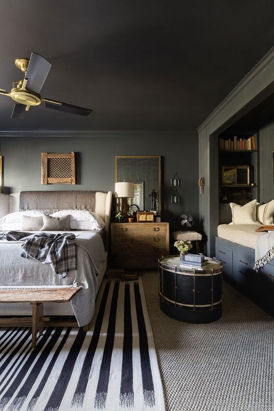 a moody bedroom with grey walls and a black ceiling, a niche daybed with bookshelves, a bed with neutral bedding, stained furniture and a catchy drum table