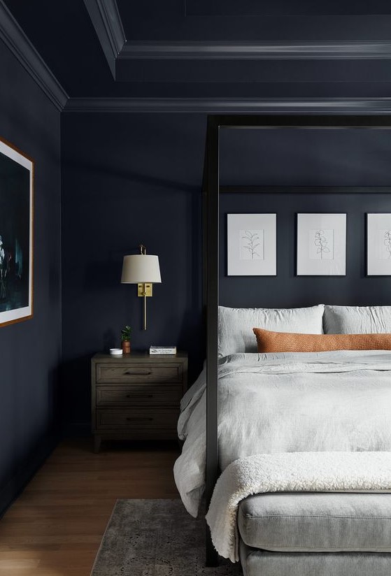 a moody bedroom with navy walls, a cnaopy bed, neutral textiles and a gallery wall, lamps on the nightstands