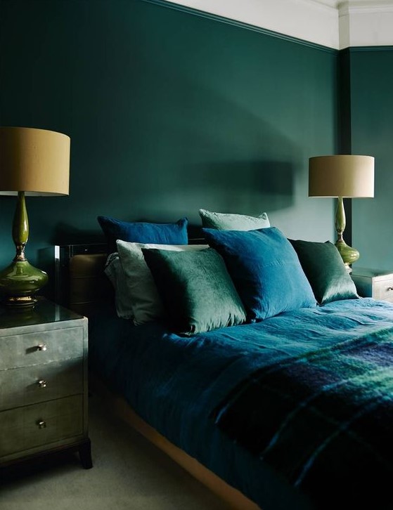 a moody refined bedroom with hunter green walls, green nightstands, green and blue bedding and refined lamps