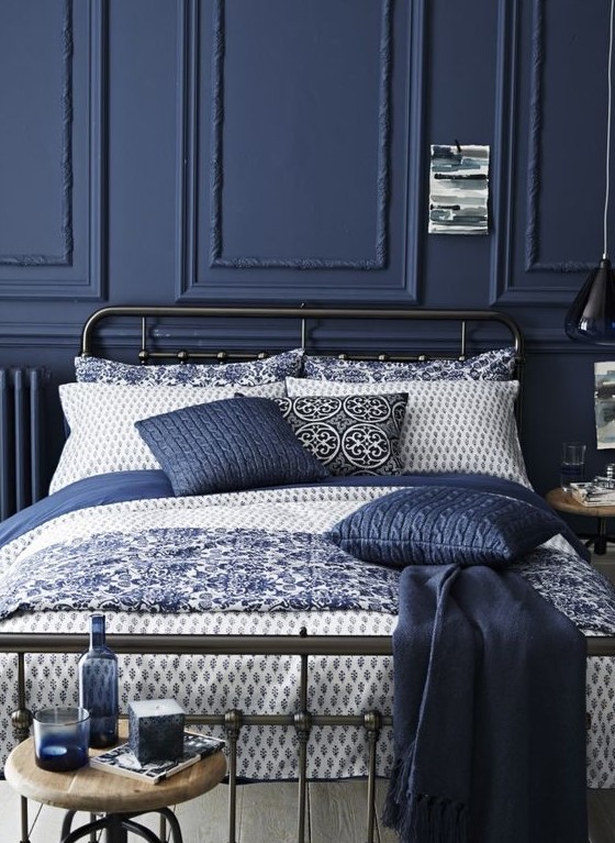 a moody refined bedroom with navy paneling, a black metal bed, vintage stools and navy bedding