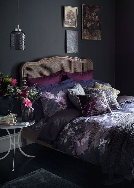 a moody vintage bedroom with black walls, a rattan bed, a gallery wall, a little nightstand and a pendant lamp