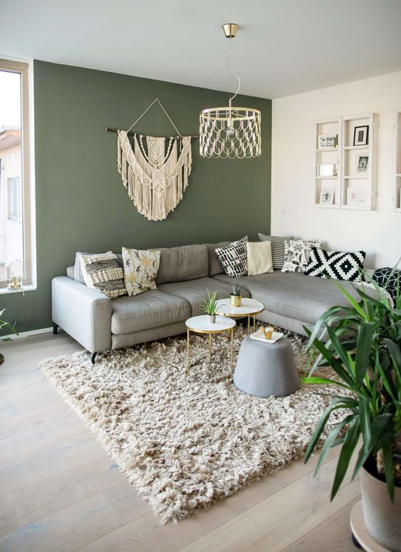 a pretty living room with a green accent wall, a grey sectional, some boho decor and printed pillows, a fluffy rug and coffee tables