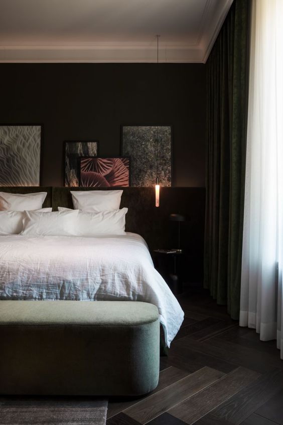 a sophisticated dark bedroom with a ledge with artwork, a bed with white bedding, a green curved bench, pendant lamps