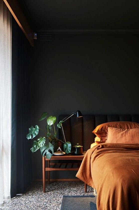 a welcoming moody bedroom with black walls and a bed, with wooden nightstands, rust-colored bedding and black curtains