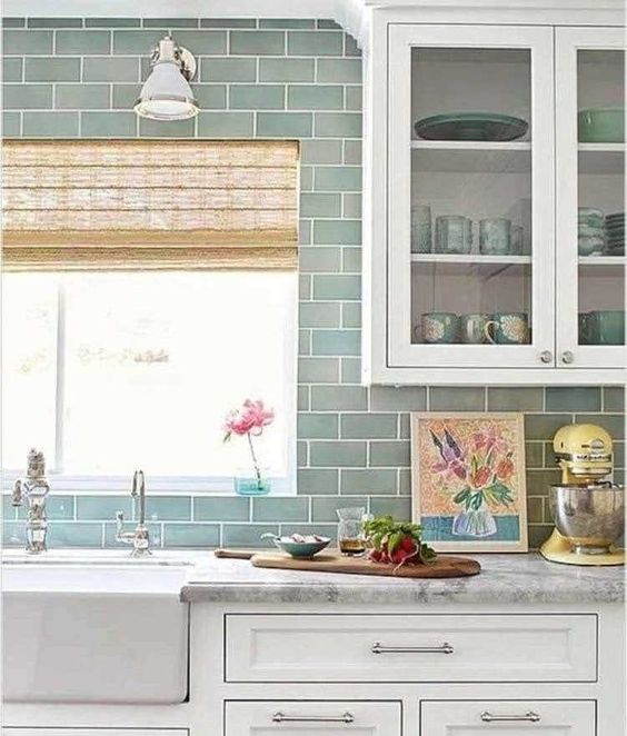 a wgute modern farmhouse kitchen wiht grey and green subway tiles, a glass storage unit, a white sink and lamps
