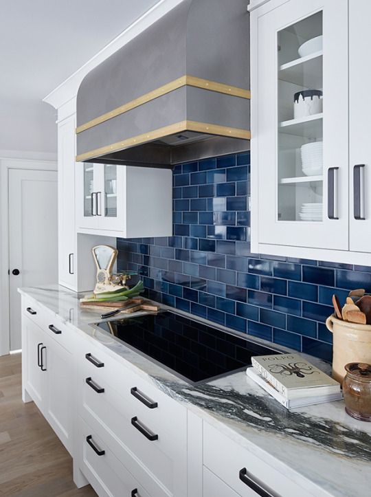 a white kitchen with a navy subway tile backsplash, a metal hood, a white stone countertop is super chic