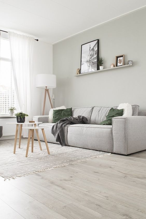an airy living room with a dove grey accent wall and a matching low sofa, green pillows, a ledge gallery wall, a floor lamp and a couple of coffee tables