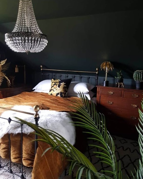 an elegant moody bedroom with a metal bed, a wooden nightstand, a statement crystal chandelier and potted plants