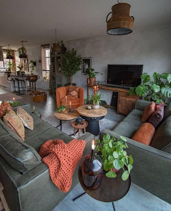 an industrial living room with grey plaster walls and a floor, green leather sofas, orange pillows and a chair, some coffee tables with greenery