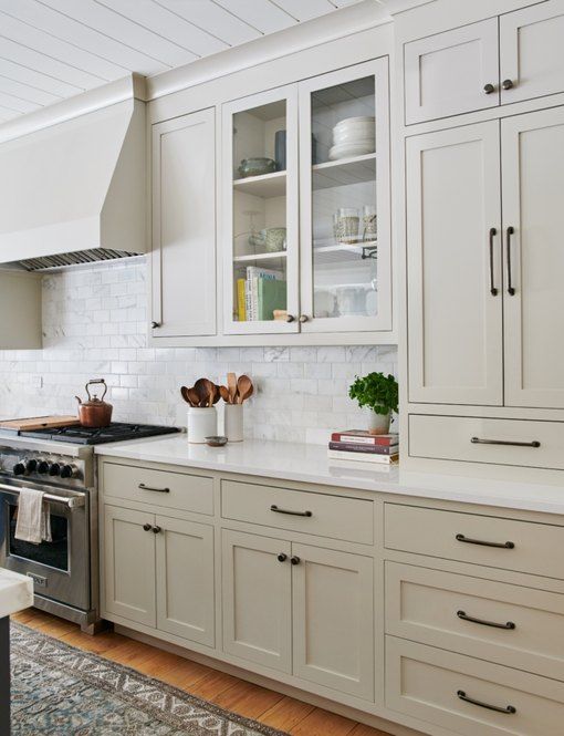 an off-white farmhouse kitchen with shaker cabinets, a white marble subway tile backsplash and a large hood