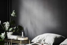 an elegant moody bedroom with graphite walls and a refined gold and glass tiered nightstand plus a potted plant