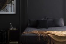 a sophisticated bedroom with black walls, a black canopy bed with black and gold bedding, a couple of nightstands and a gorgeous artwork