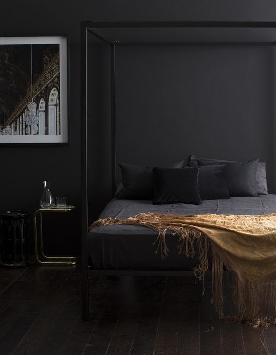 a sophisticated bedroom with black walls, a black canopy bed with black and gold bedding, a couple of nightstands and a gorgeous artwork