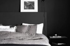 a minimalist bedroom design with matte black walls, a black bed with monochromatic bedding, a nightstand and a black lamp plus an artwork