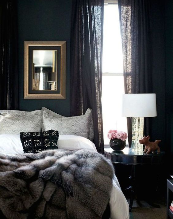 moody bedroom with black curtains, a fur blanket and a framed mirror