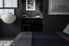 a moody bedroom with black walls and a floor, a bed with dark bedding, cool gallery walls and a floor lamp that bring a touch of something light to the dark space