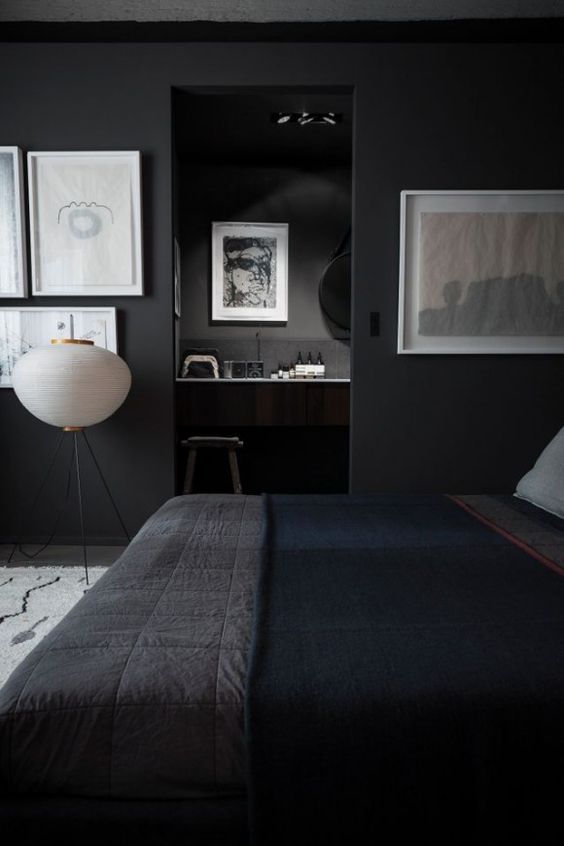 a moody bedroom with black walls and a floor, a bed with dark bedding, cool gallery walls and a floor lamp that bring a touch of something light to the dark space