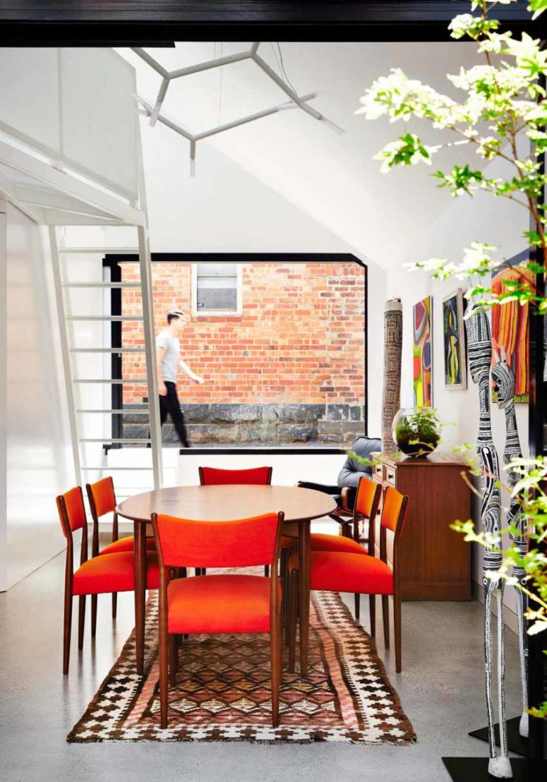 The dining space is mid century modern, with orange chairs and a round table, a cool rug makes the space inviting The dining space is mid-century modern, with orange chairs and a round table, a cool rug makes the space inviting