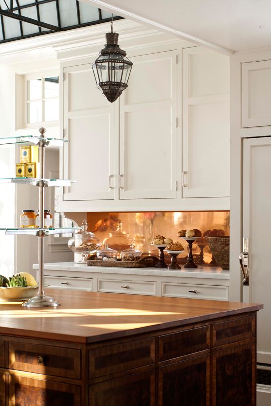 plain white cabinets are glamed up with a polished copper backsplash