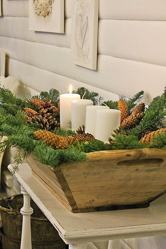 a wooden dough bowl with evergreens, pinecones and pillar candles