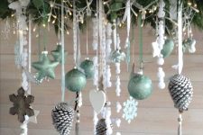 a Christmas chandelier with evergreens and greenery, lights, light green ornaments, wooden snowflakes and hearts and snowy pinecones