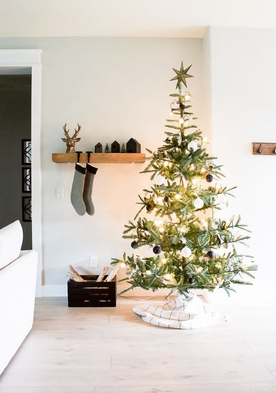 a Christmas tree with lights and black and white ornaments, black houses and stockings on the mantel and a crate with firewood