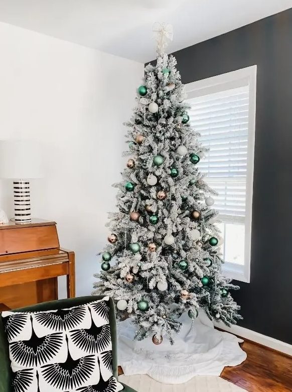 a beautiful flocked Christmas tree decorated with white, copper and green ornaments and a green chair for the holidays