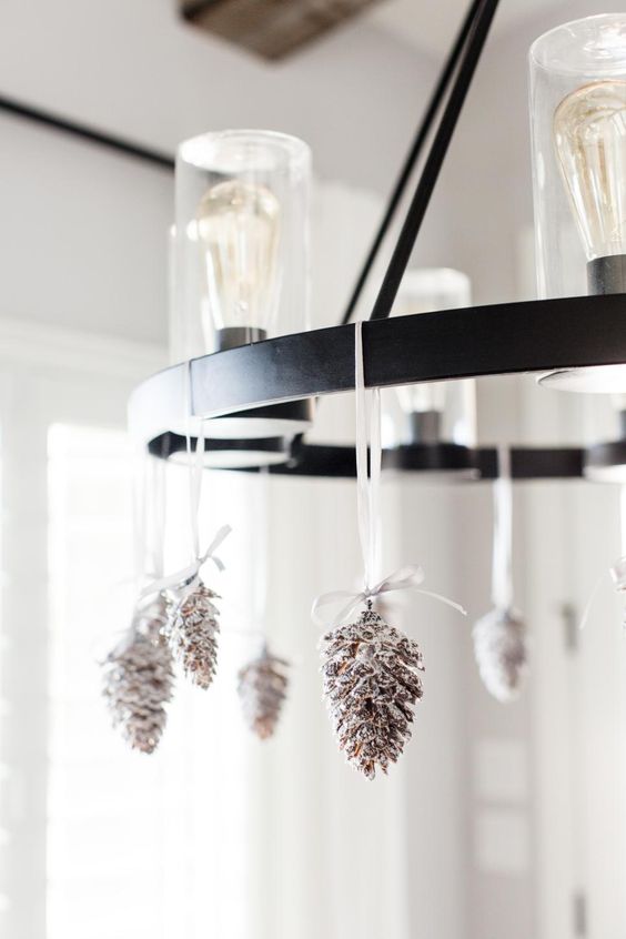 a bulb chandelier decorated with snowy pinecones is a cool and chic idea for the holidays, it's quite rustic