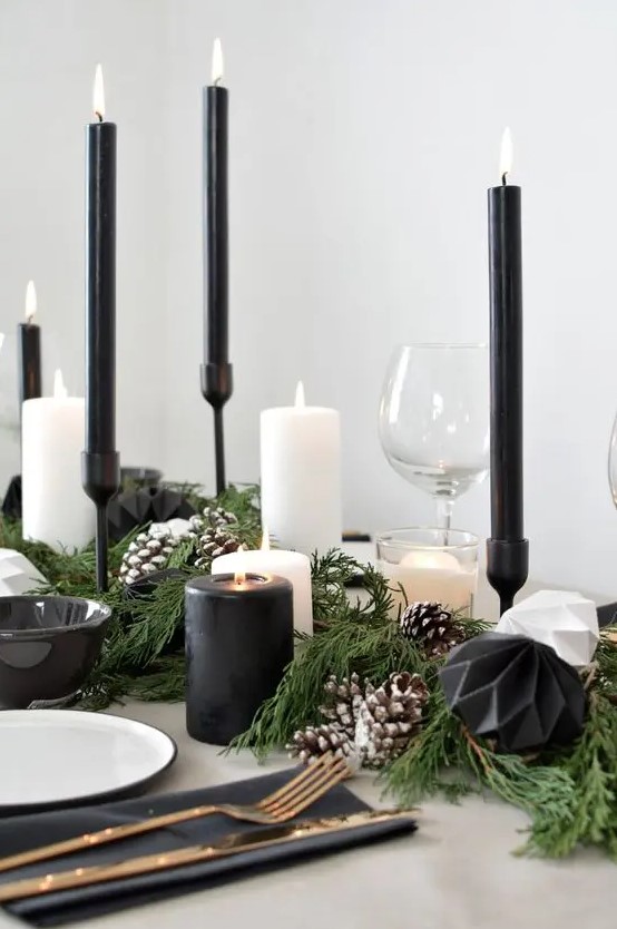 a contrasting Christmas table with an evergreen runner with snowy pinecones, black and white faceted ornaments, black and white candles and white plates plus black napkins