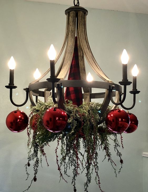 a cool vintage chandelier with greenery and red ornaments is a stylish idea for Christmas, it looks very festive