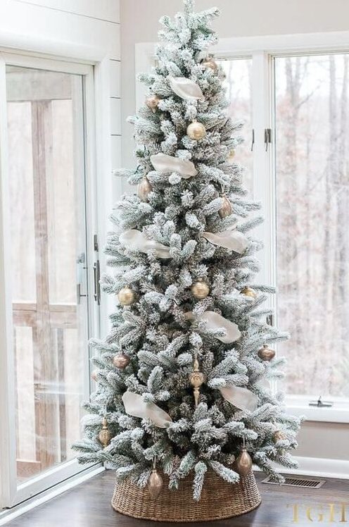 a flocked Christmas tree decorated with white and gold ornaments, with white ribbon, placed in a basket for a farmhouse feel