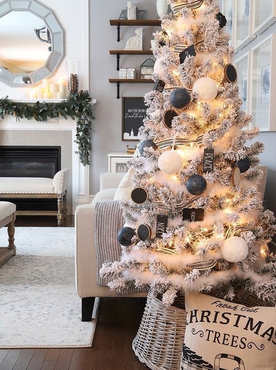 a flocked Christmas tree decorated with white fur garlands, black and white ornaments, chalkboard ones and with a basket base cover