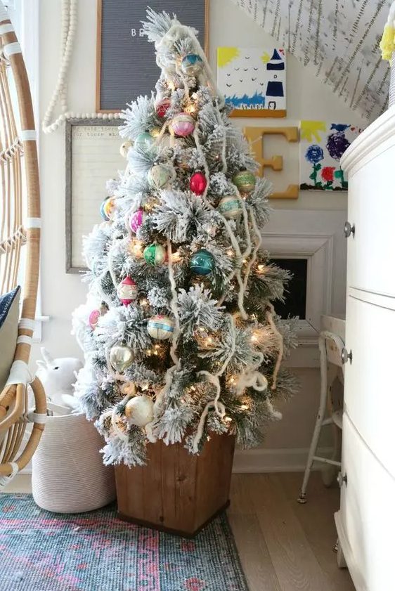 a flocked Christmas tree in a wooden box and decorated with colorful ornaments with a vintage feel