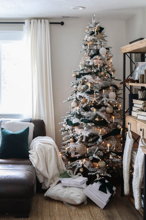 a flocked Christmas tree with lights, candles, metallic and white ornaments and black ribbon is elegant and glam