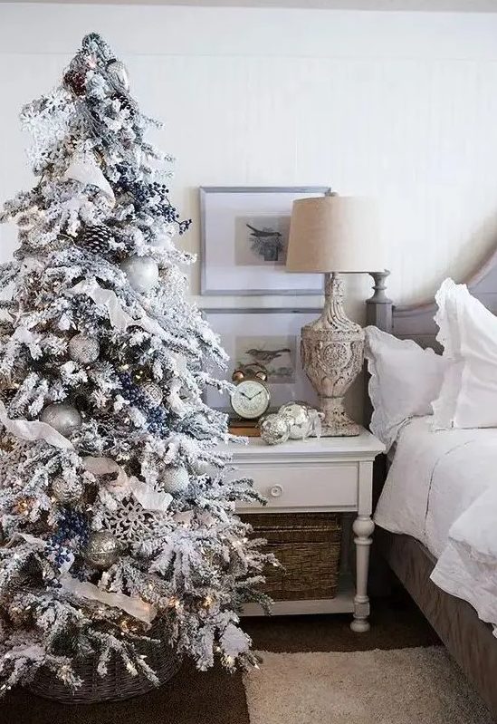 a flocked Christmas tree with privet berries, snowflakes, ribbons, white and silver ornaments and pinecones plus lights is amazing