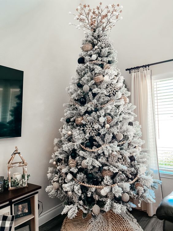 a flocked Christmas tree with wooden beads, snowflakes, branches on top and some black and metallic ornaments