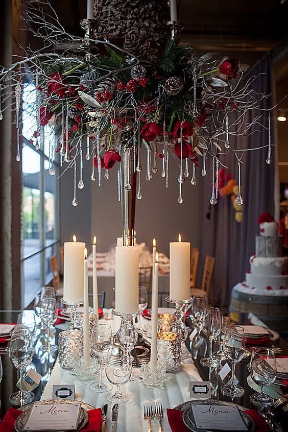 a glam Christmas chandelier with branches, evergreens, red roses, snowy pinecones and crystals as icicles