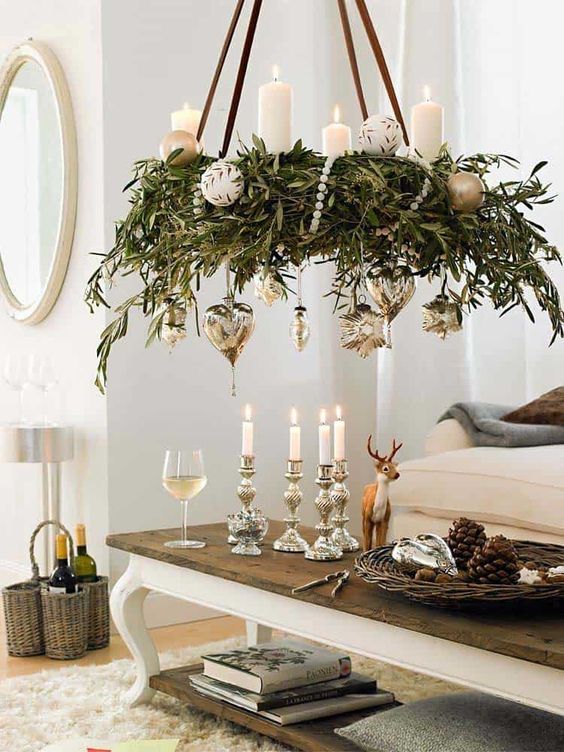 a lovely wreath holiday chandelier with greenery, beads, pillar candles and silver and white ornaments is adorable