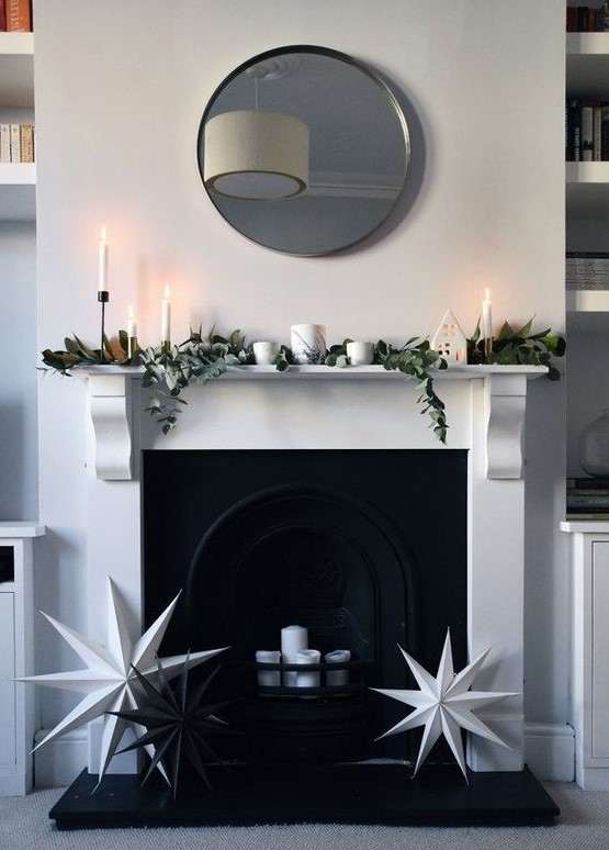 a minimalist Christmas mantel decorated with magnolia leaves and eucalyptus plus white candles and black and white stars