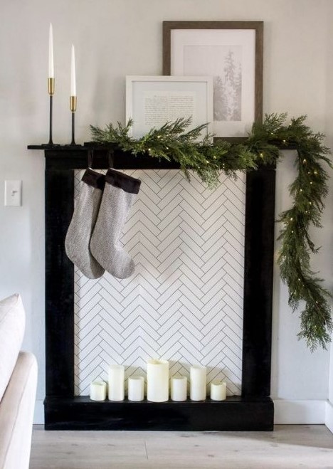 a minimalist faux fireplace with candles, simple grey stockings and an evergreen garland with lights