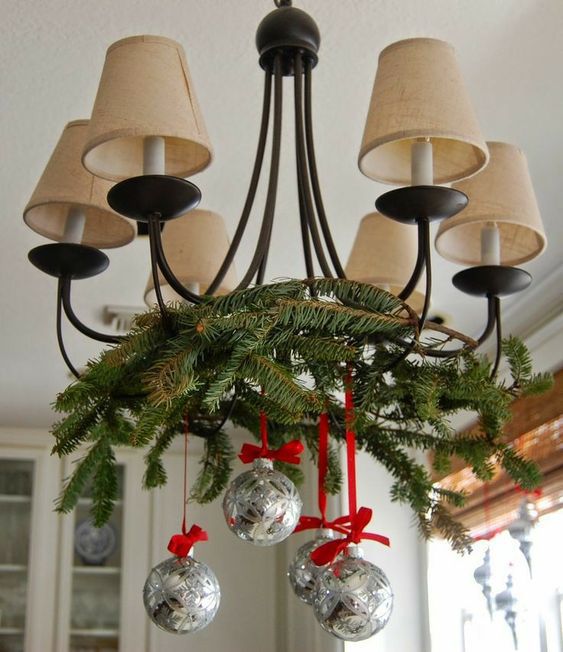 a pretty vintage chandelier with lampshades decoraed with evergreens, silver ornaments and red ribbon is a cool and chic idea