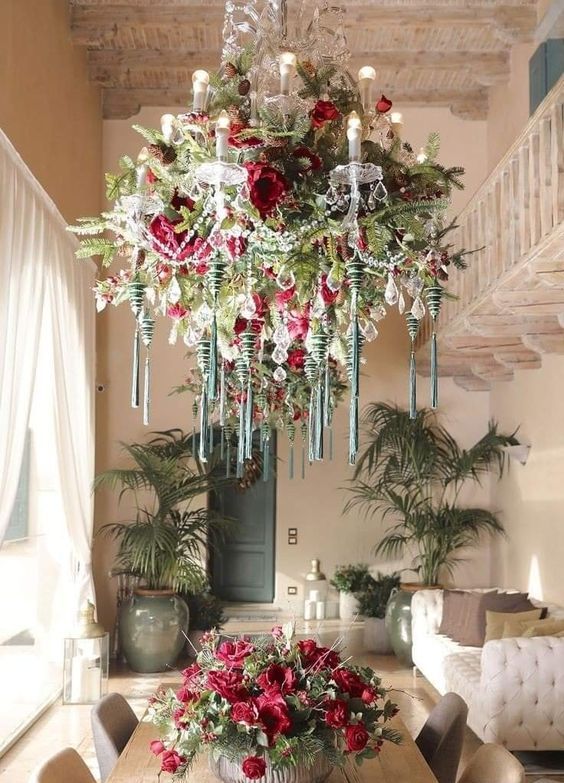 a refined crystal chandelier covered with greenery, red blooms, green ornaments with tassels and some crystals
