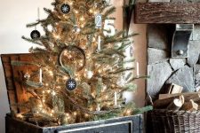 a rustic Christmas tree with lights, chalkboard ornaments, numbers, a stick star placed into a black chest is a cozy and cool idea