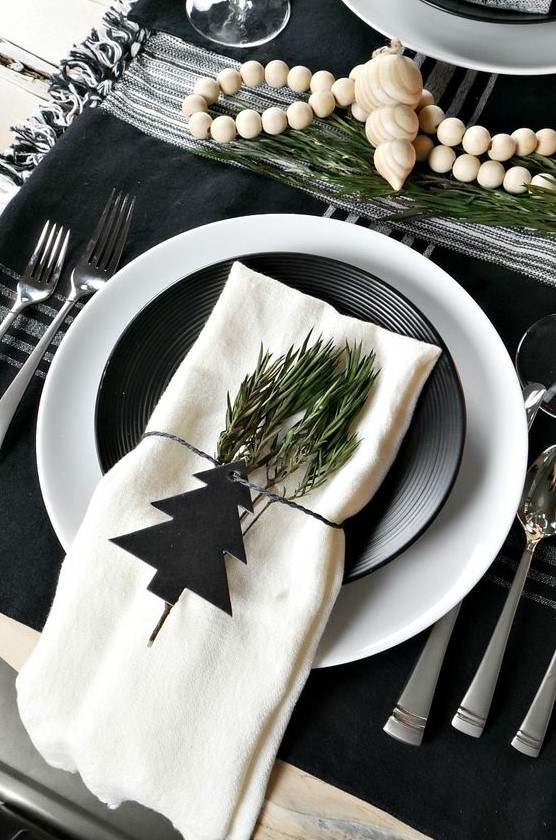 a stylish black and white Scandinavian Christmas tablescape with black and white linens, plates, greenery and wooden beads is amazing