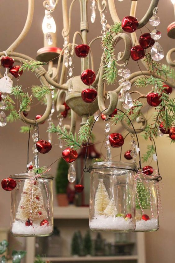 a vintage chandelier decorated with red bells, evergreens and mini terrariums hanging on it is fab