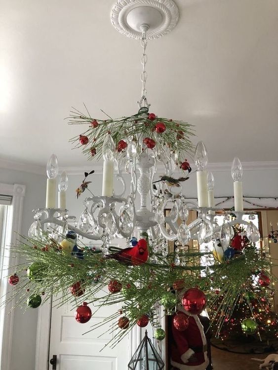 a vintage chandelier with evergreens, red and green ornaments is a chic and beautiful decor idea for the holidays