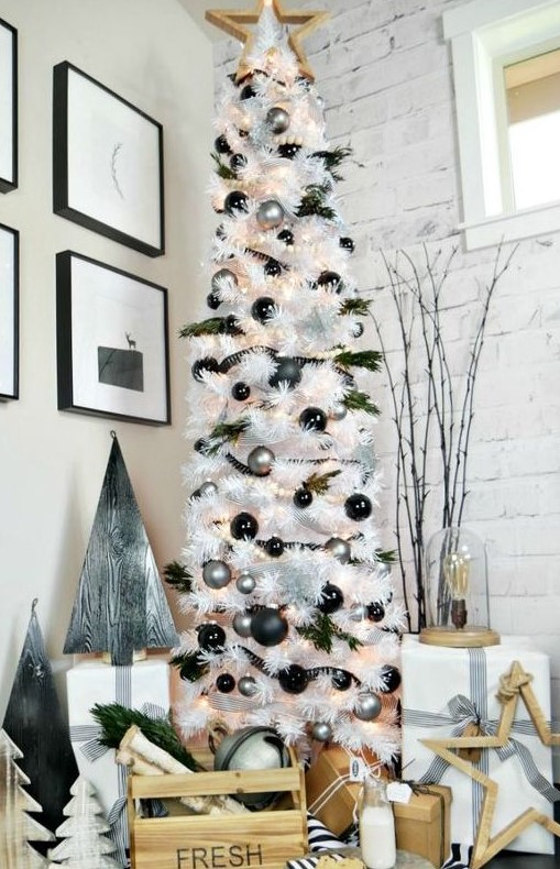 a white Christmas tree decorated with black and silver ornaments, evergreens, snowflakes, a wooden star topper