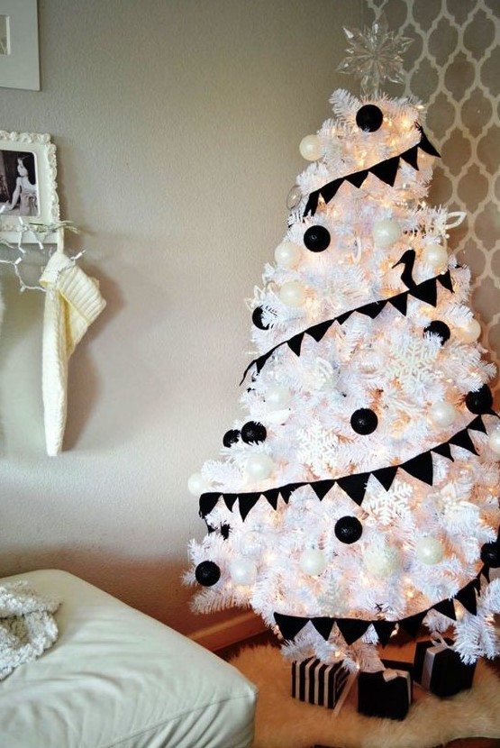 a white Christmas tree decorated with black and white ornaments, with snowflakes and lights plus a clear snowflake topper