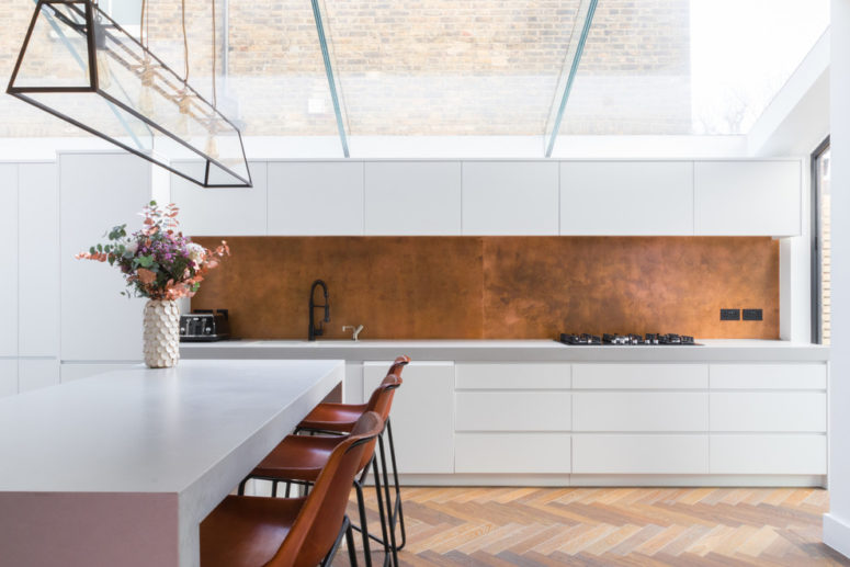 a pure white kitchen cabinets, a copper backsplash and wooden flooring is an ultimate mix for a contemporary yet cozy kitchen design