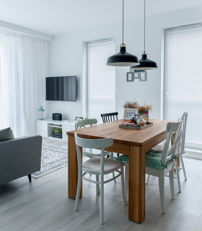 The dining zone flows into a small living room with a grey sofa and glass doors that lead to the bedroom